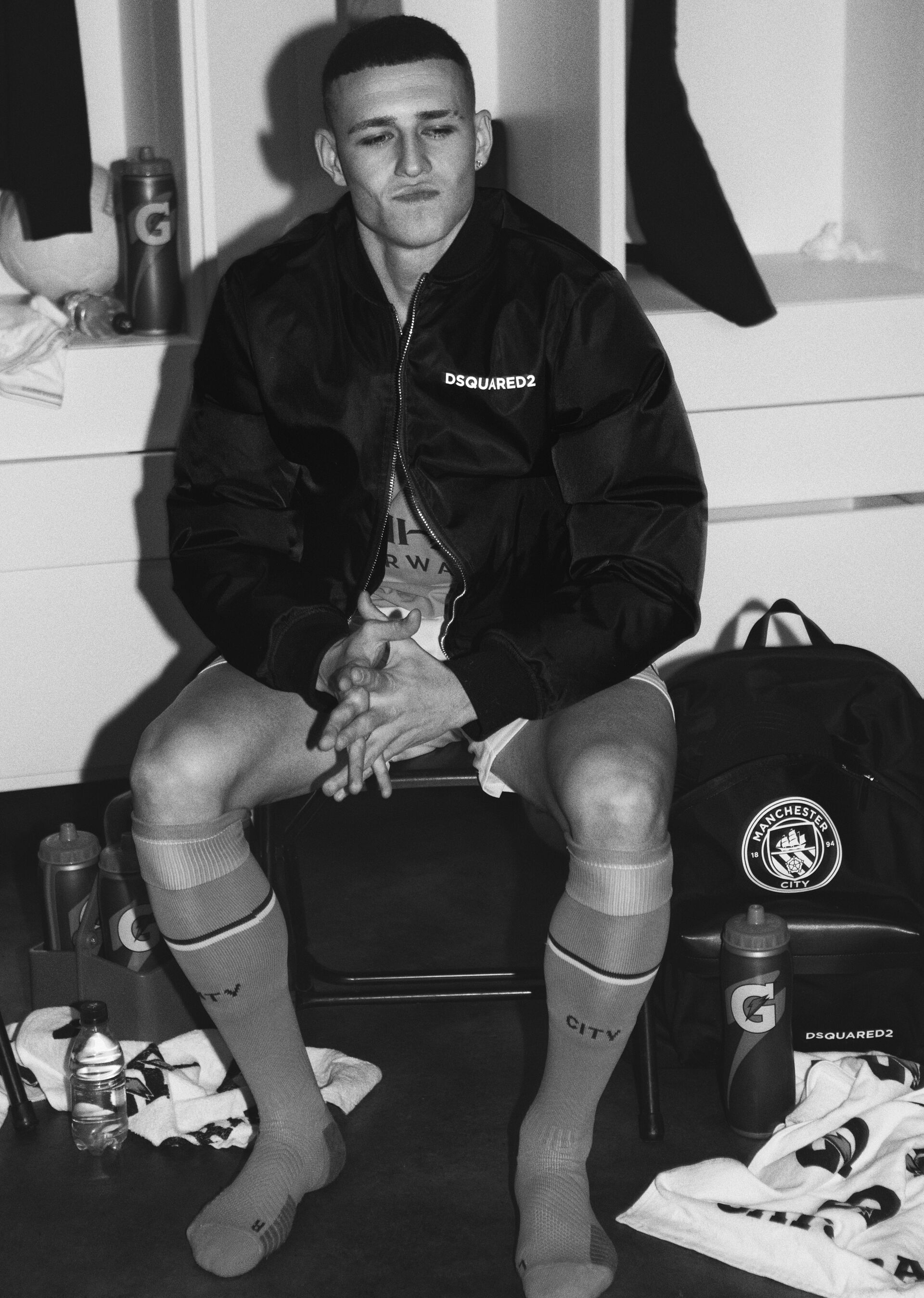 Picture in black and white of phil foden in the locker room wearing a black bomber jacket from the new dsquared2 x manchester city capsule collection