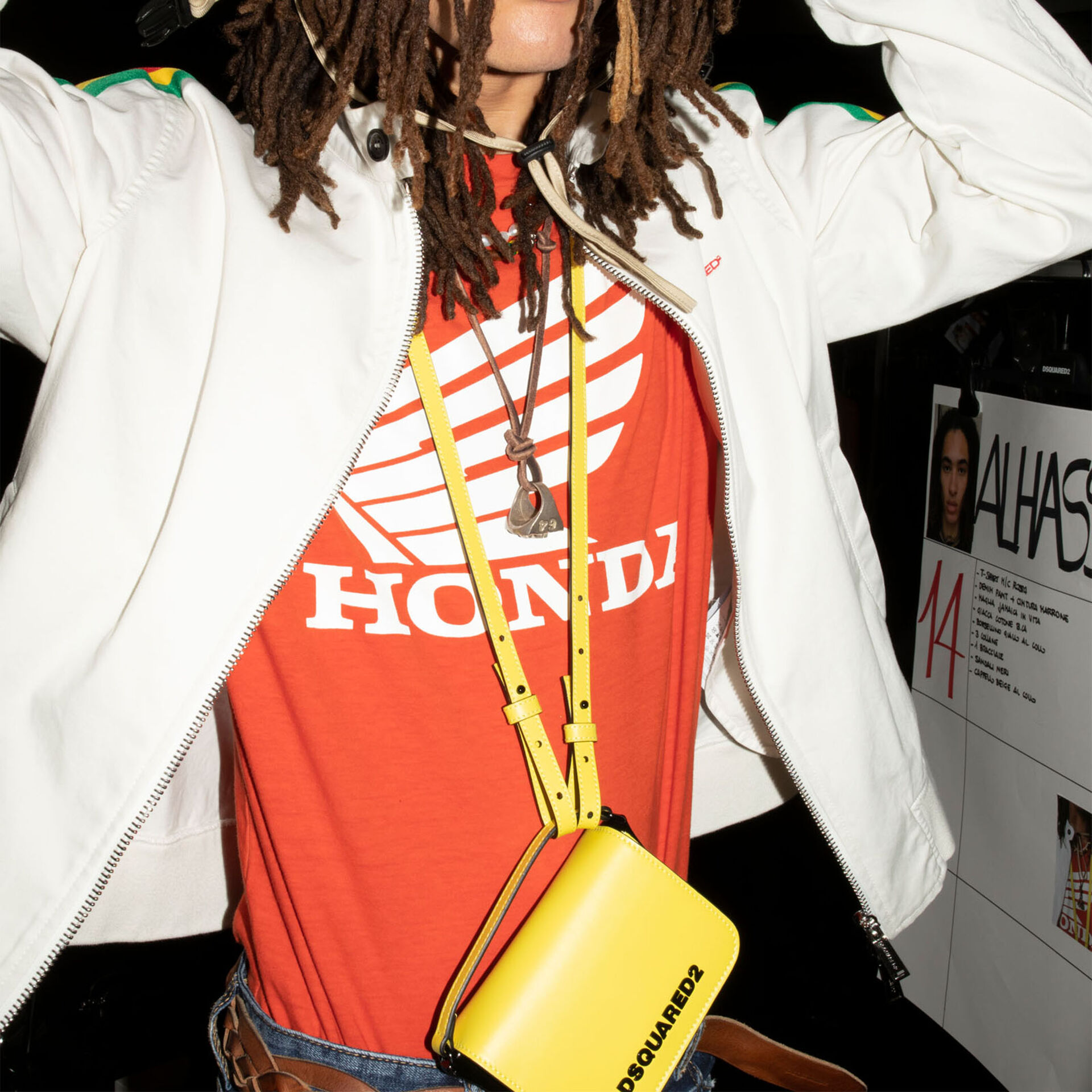 man wearing a white leather jacket, with yellow bag hanging from his neck and red t-shirt with white Honda logo. 