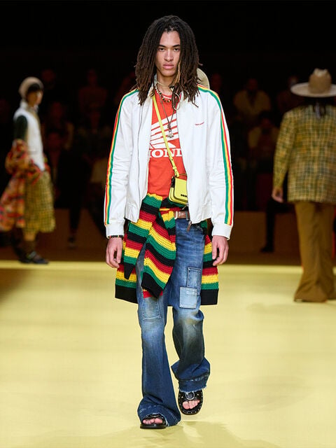 Man with long hair, white jacket and jamaican style pullover wrapped around his waist. 